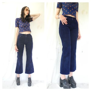 Puede incluir: Una mujer con una camisa de estampado azul y marrón y pantalones acampanados de pana azul oscuro. Lleva zapatos negros con tacón grueso.