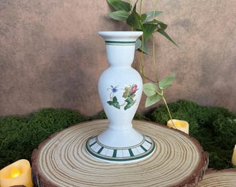 Könnte beinhalten: Ein weißer Kerzenhalter aus Keramik mit ausgestelltem Fuß und verjüngtem Hals. Das Stück zeigt ein grün-weißes geometrisches Randmuster oben und unten sowie ein zentrales Blumenmotiv mit einer kleinen rosa Rose und einer blauen Blume.