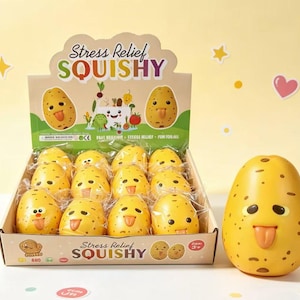 May include: A cardboard display box containing twelve yellow potato-shaped stress relief squishy toys, each featuring a brown-spotted surface and a protruding tongue. The box is labeled Stress Relief SQUISHY with cartoon vegetable graphics.
