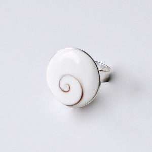May include: A white shell ring with a silver band. The shell has a brown spiral pattern.