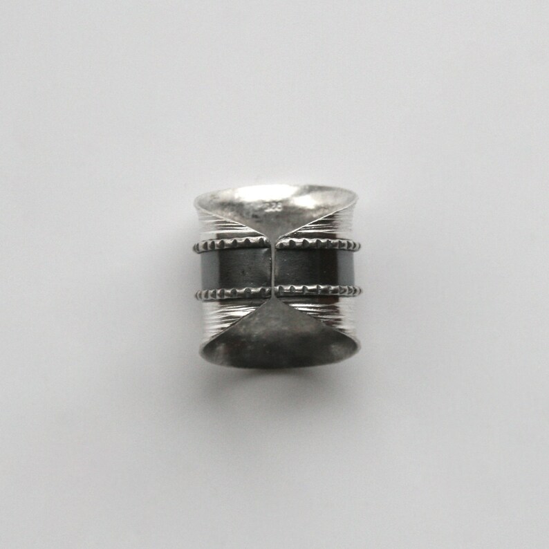 May include: A silver ring with two black bands and a textured design.