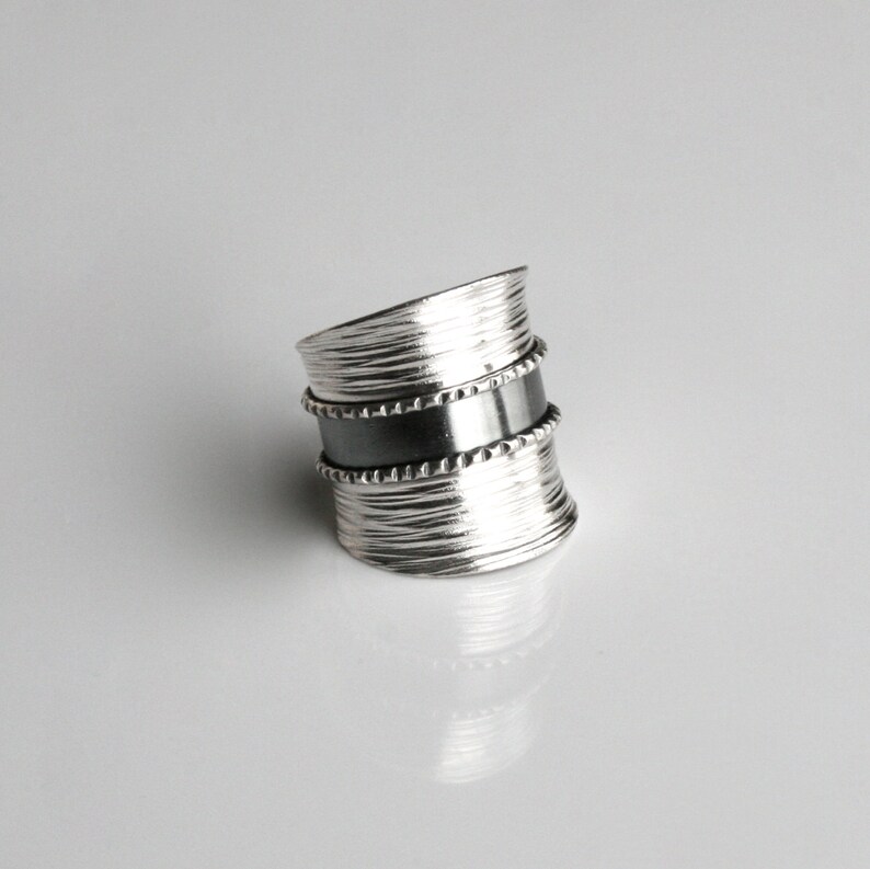 May include: A silver ring with a textured band and a black band with a beaded edge.