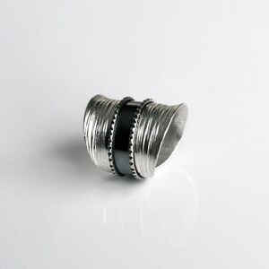 May include: A silver ring with a textured, wavy design and a black band in the center.