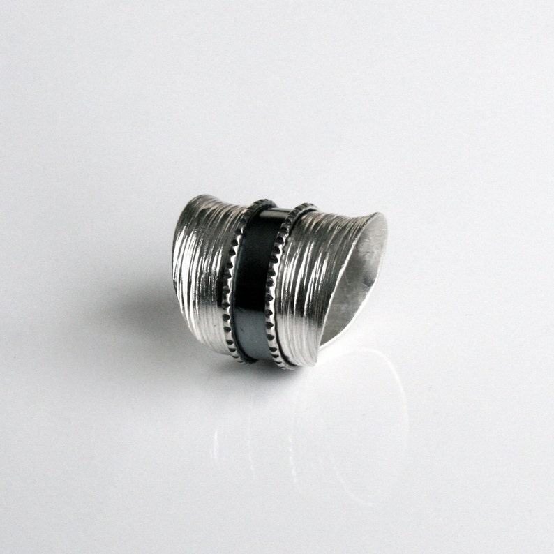 May include: A silver ring with a textured, wavy design and a black band in the center.