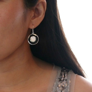 May include: Silver dangle earrings with a white oval stone set in a black circle.