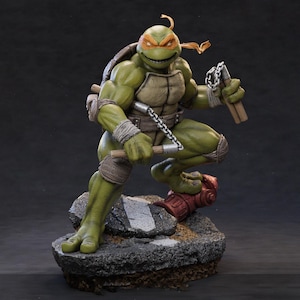 May include: A green anthropomorphic turtle action figure with an orange eye mask, muscular build, and a brown shell. The figure holds silver nunchucks with wooden handles and stands on a textured base featuring a red fire hydrant and asphalt.