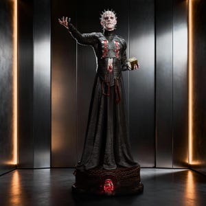 May include: A detailed collectible statue of Pinhead featuring a pale head with silver pins, wearing a black leather-textured robe with red lacing details. The figure holds a gold puzzle box and stands on a dark, ornate base with a glowing red light.