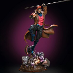 May include: A detailed collectible statue of a male character with brown hair, wearing a long brown trench coat over a pink chest piece and black pants. The figure holds a long staff above its head and stands on a rocky, metallic base.