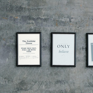 Op de afbeelding: Drie zwarte rechthoekige lijsten met witte prints. De linker print lijkt op een krant genaamd The Faithful Times met de tekst Fear Thou Not; For I Am With Thee. De middelste print toont Only believe. De rechter print bevat een veer.