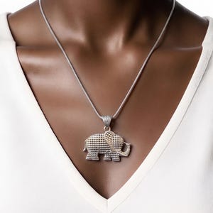 May include: A silver-toned elephant pendant necklace featuring a textured, dotted surface on the body and a contrasting gold-toned ear detail. The pendant hangs from a thin, flexible silver-toned chain against a plain white fabric background.