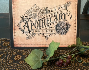 May include: Apothecary sign with a vintage design. The sign features the words "Powder Elixir Potions" and "Black Rose" above the word "Apothecary". The sign has a black frame and a distressed background. A sprig of grapes and leaves is in the foreground.