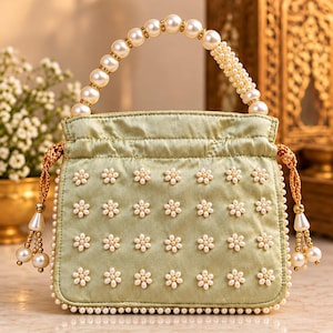 May include: A light green satin drawstring handbag featuring a handle made of large white pearls. The front of the bag is decorated with a grid of small white pearl flower embellishments. Gold braided drawstrings with pearl tassels hang from the sides.