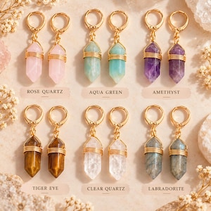 Puede incluir: Seis pares de pendientes de aro dorados con colgantes de cristal hexagonal envueltos en alambre de cuarzo rosa, verde agua, amatista, ojo de tigre, cuarzo claro y labradorita, etiquetados con su nombre de piedra.