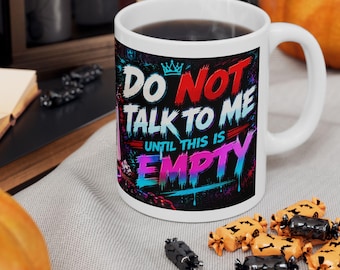 May include: A white ceramic mug featuring a colorful graphic print with the text DO NOT TALK TO ME UNTIL THIS IS EMPTY. The design includes a small crown icon and vibrant paint drip effects in shades of red, blue, and purple against a dark background.