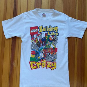 May include: White t-shirt with a colorful LEGO graphic that says "Building Like Crazy".