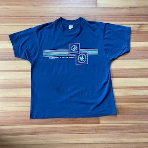 Puede incluir: Una camiseta azul marino con el texto "Girl Scouts National Center West" y un logotipo de Girl Scout.