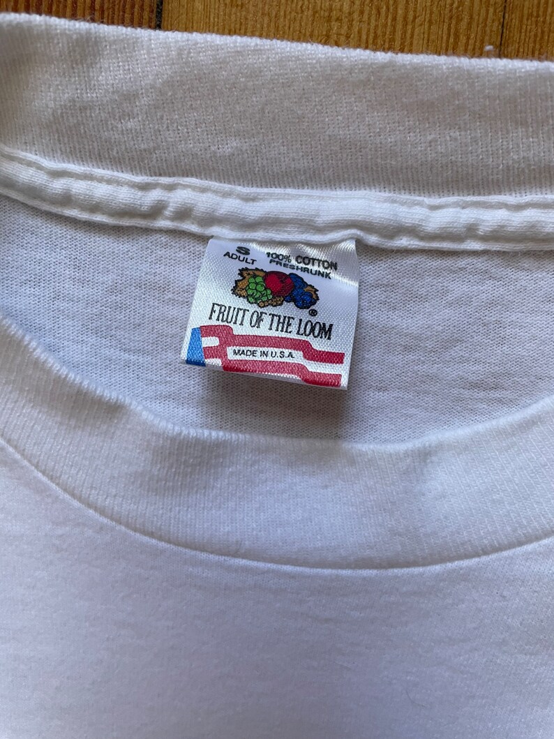 May include: White Fruit of the Loom tag with a red, white, and blue American flag. The tag says "Adult S 100% Cotton Preshrunk Fruit of the Loom Made in U.S.A."