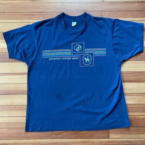Puede incluir: Una camiseta azul marino con un logotipo de Girl Scouts National Center West. El logotipo presenta una silueta blanca de una ni&ntilde;a montando a caballo con las palabras "Girl Scouts National Center West" impresas debajo.