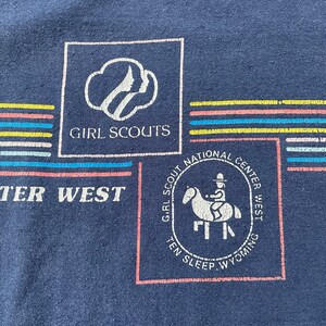 Puede incluir: Una camiseta azul marino con un logotipo de Girl Scouts y el texto "Girl Scouts National Center West Ten Sleep Wyoming".