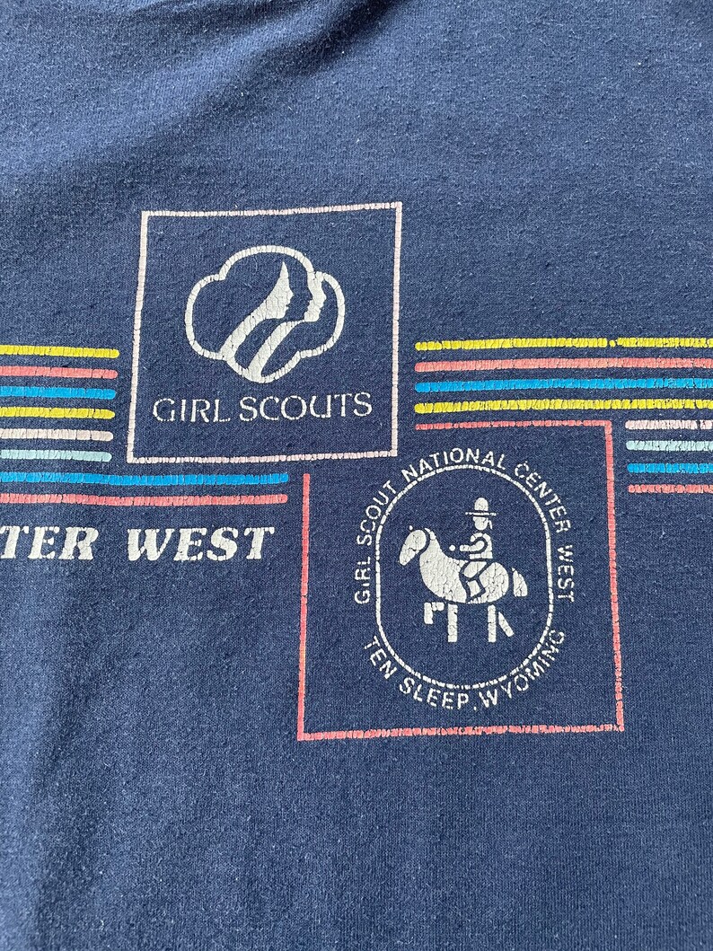 Puede incluir: Una camiseta azul marino con un logotipo de Girl Scouts y el texto "Girl Scouts National Center West Ten Sleep Wyoming".