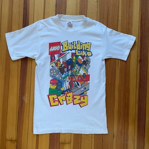 May include: White t-shirt with a colorful LEGO graphic that says "Building Like Crazy".