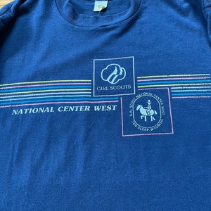 Puede incluir: Una camiseta azul marino con un logotipo de Girl Scouts y el texto "National Center West" y "Girl Scout National Center West Ten Sleep Wyoming".