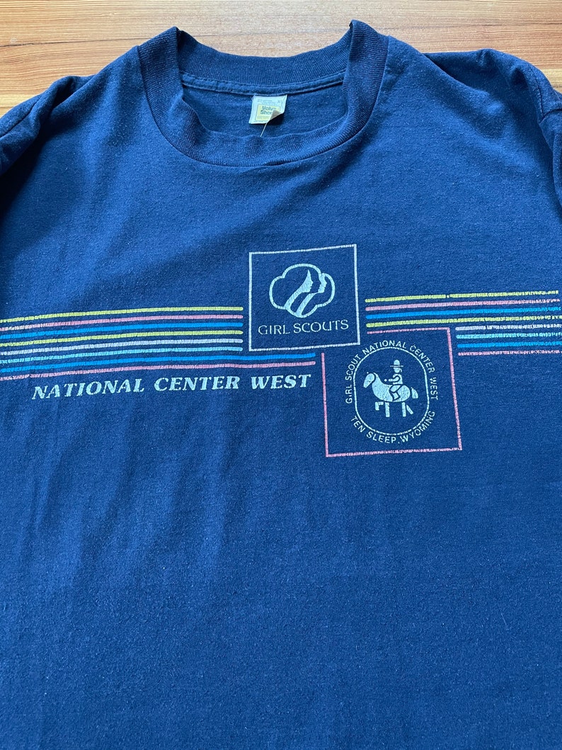 Puede incluir: Una camiseta azul marino con un logotipo de Girl Scouts y el texto "National Center West" y "Girl Scout National Center West Ten Sleep Wyoming".