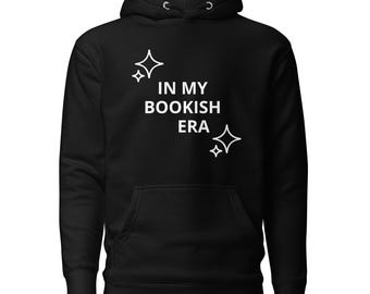 May include: A black hooded sweatshirt featuring the white text IN MY BOOKISH ERA printed on the chest. The design includes two white four-pointed star icons, one positioned above the text and one below, centered on the front of the garment.