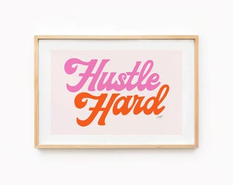 May include: Framed art print with the words "Hustle Hard" in pink and orange script lettering on a light pink background. The artwork is in a light wood frame.