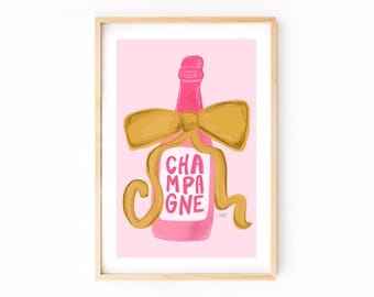 Puede incluir: Impresión enmarcada de una botella de champán rosa con un lazo dorado y la palabra "CHAMPAGNE" en blanco. El fondo es rosa suave. La obra de arte está en un marco de madera.