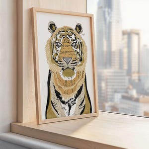 Puede incluir: Una impresi&oacute;n art&iacute;stica enmarcada que presenta la cara de un tigre. El pelaje del tigre es una mezcla de dorado, marr&oacute;n y negro, con la cara y la melena que incorporan texto de p&aacute;ginas de libros antiguos. La obra de arte se muestra en un marco de madera clara.