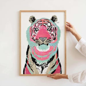 Puede incluir: Una impresi&oacute;n art&iacute;stica enmarcada con una ilustraci&oacute;n de un tigre colorido. La cara del tigre es predominantemente rosa, con detalles en turquesa, negro y blanco. La obra de arte est&aacute; sostenida, mostrando el marco de madera y el dise&ntilde;o vibrante.