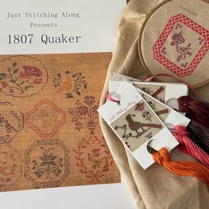 Puede incluir: Kit de punto de cruz con un diseño de muestrario con motivos florales y de pájaros. El kit incluye un patrón impreso, hilo de bordar en varios colores y un bastidor de bordado de madera. El texto "1807 Quaker" es visible.