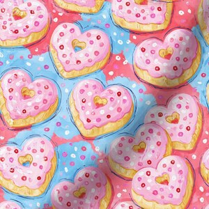 May include: A repeating pattern of heart-shaped donuts with light pink icing and red sprinkles on a light blue background with scattered pink and white dots. Each donut features a golden-brown fried dough base and a central heart-shaped hole.