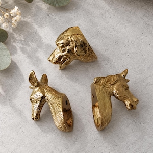 May include: Three gold-toned metal cabinet knobs shaped like animal heads. The set includes a dog head, a donkey head, and a horse head, each featuring detailed textures and a single mounting hole on the flat back side for attachment.