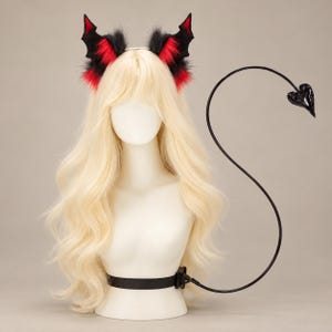 May include: A set featuring a headband with black and red faux fur bat-like ears and a long, thin black tail with a heart-shaped tip. The tail is attached to a black belt, displayed on a mannequin with long, wavy blonde hair.