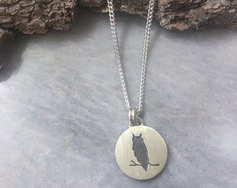 May include: A silver chain necklace with a round pendant featuring a cutout silhouette of an owl perched on a branch.