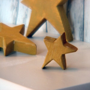 May include: Three wooden stars in a light brown color. The stars are arranged on a white surface.