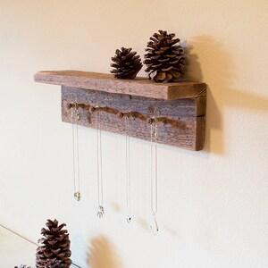 May include: Rustic wooden shelf with a branch-like design for hanging necklaces. The shelf has a natural wood finish and is decorated with pine cones.