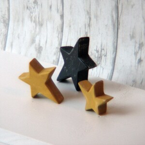 May include: Three wooden stars, one black and two gold, arranged on a white surface.