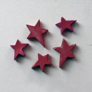 May include: Five red star-shaped ornaments with a slightly textured surface. The stars are arranged in a semi-circle on a white background.