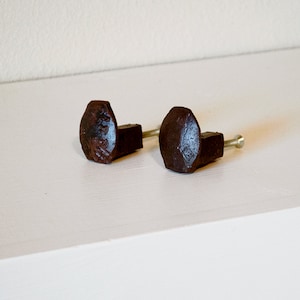 May include: Two brown metal cabinet knobs with a hexagonal shape and a screw on the side.