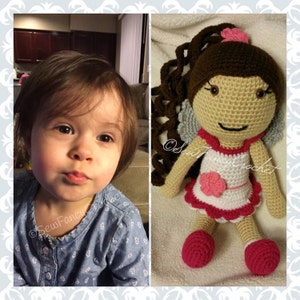 May include: A crochet doll with brown hair and a pink flower on top. The doll wears a white dress with pink trim and a pink flower on the front. The doll has gray wings and pink shoes. The image also includes a young child.