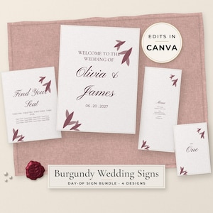 May include: A set of four white wedding signs with burgundy leaf accents and black text. The signs include a welcome sign for Olivia and James, a seating chart, a menu, and a table number. A burgundy wax seal is placed near the signs.