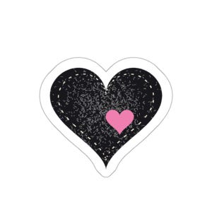 Op de afbeelding: Een zwarte hartvormige sticker met een textuurrijk, gespikkeld oppervlak en een witte stippellijn als rand. Een kleiner, effen roze hartje is geplaatst aan de rechteronderkant van het grote zwarte hart voor een gelaagd effect.