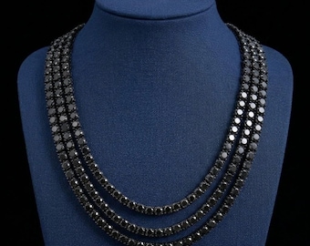 May include: A triple-strand necklace featuring round, faceted black stones set in a continuous metal chain. The three strands are layered, creating a uniform circular drape with a dark, reflective finish across all the individual stone settings.