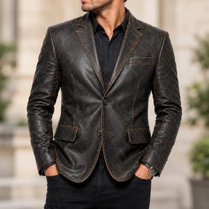 Könnte beinhalten: Ein dunkelbrauner Blazer aus Distressed-Leder mit steigendem Revers, zwei Knöpfen auf der Vorderseite, zwei Pattentaschen und einer Brusttasche. Die Jacke wird über einem schwarzen Hemd mit Kragen und einer schwarzen Hose getragen.