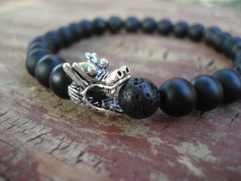 May include: Black beaded bracelet with a silver dragon charm and a black lava rock bead.