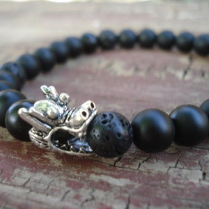May include: Black beaded bracelet with a silver dragon charm. The beads are made of black lava rock and onyx.