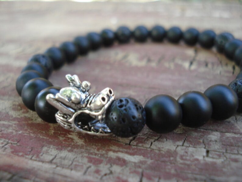 May include: Black beaded bracelet with a silver dragon charm. The beads are made of black lava rock and onyx.